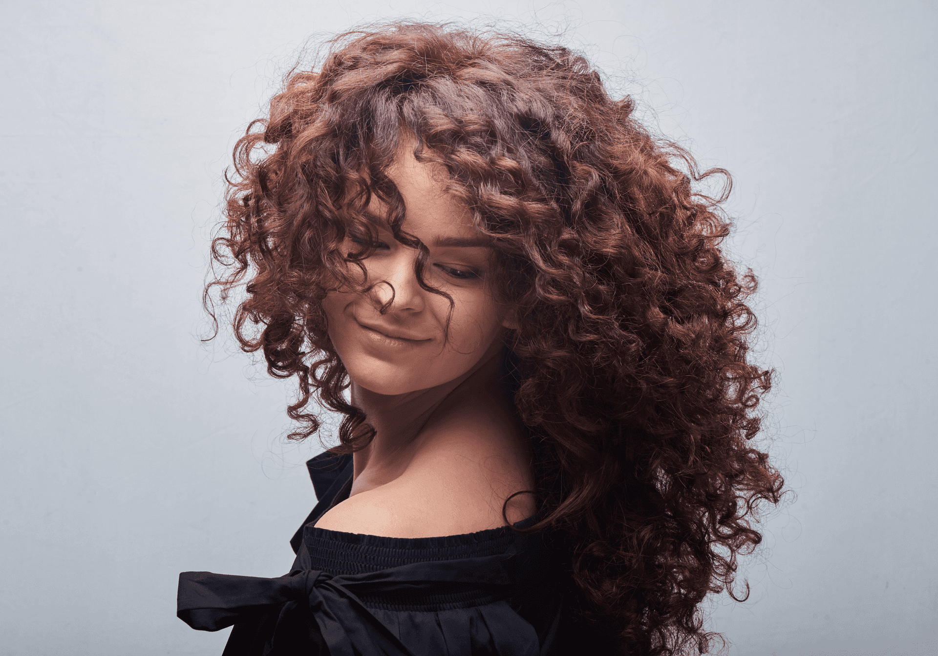 Woman with curly hair smiling with closed eyes.