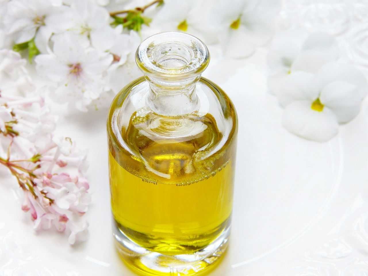 Clear glass bottle of yellow oil with white blossoms on white background.